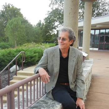 Annie Varughese MD vilkintis juodą smokingą ir varlytę, stovi priešais banerį su logotipais, įskaitant Oscars ir HeartDaHeart Foundation, oficiali renginio aplinka, neutralus ir profesionalus įspūdis, matomas tekstas: Oscars HeartDaHeart Foundation UnmaskHeartDisease