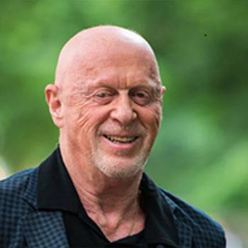 Thomas Redner MD vilkintis juodą smokingą ir varlytę, stovi priešais banerį su logotipais, įskaitant Oscars ir HeartDaHeart Foundation, oficiali renginio aplinka, neutralus ir profesionalus įspūdis, matomas tekstas: Oscars HeartDaHeart Foundation UnmaskHeartDisease