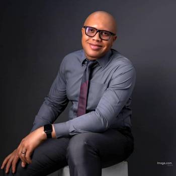 Luis Miguel Valdes MD vilkintis juodą smokingą ir varlytę, stovi priešais banerį su logotipais, įskaitant Oscars ir HeartDaHeart Foundation, oficiali renginio aplinka, neutralus ir profesionalus įspūdis, matomas tekstas: Oscars HeartDaHeart Foundation UnmaskHeartDisease